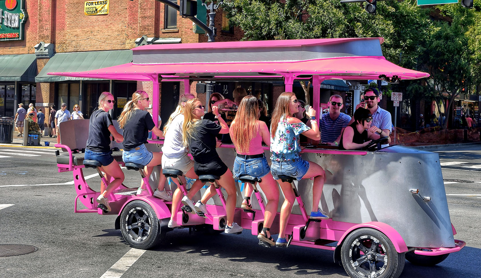 Pink 15-person party bike pedalled through a city street on a weekend package